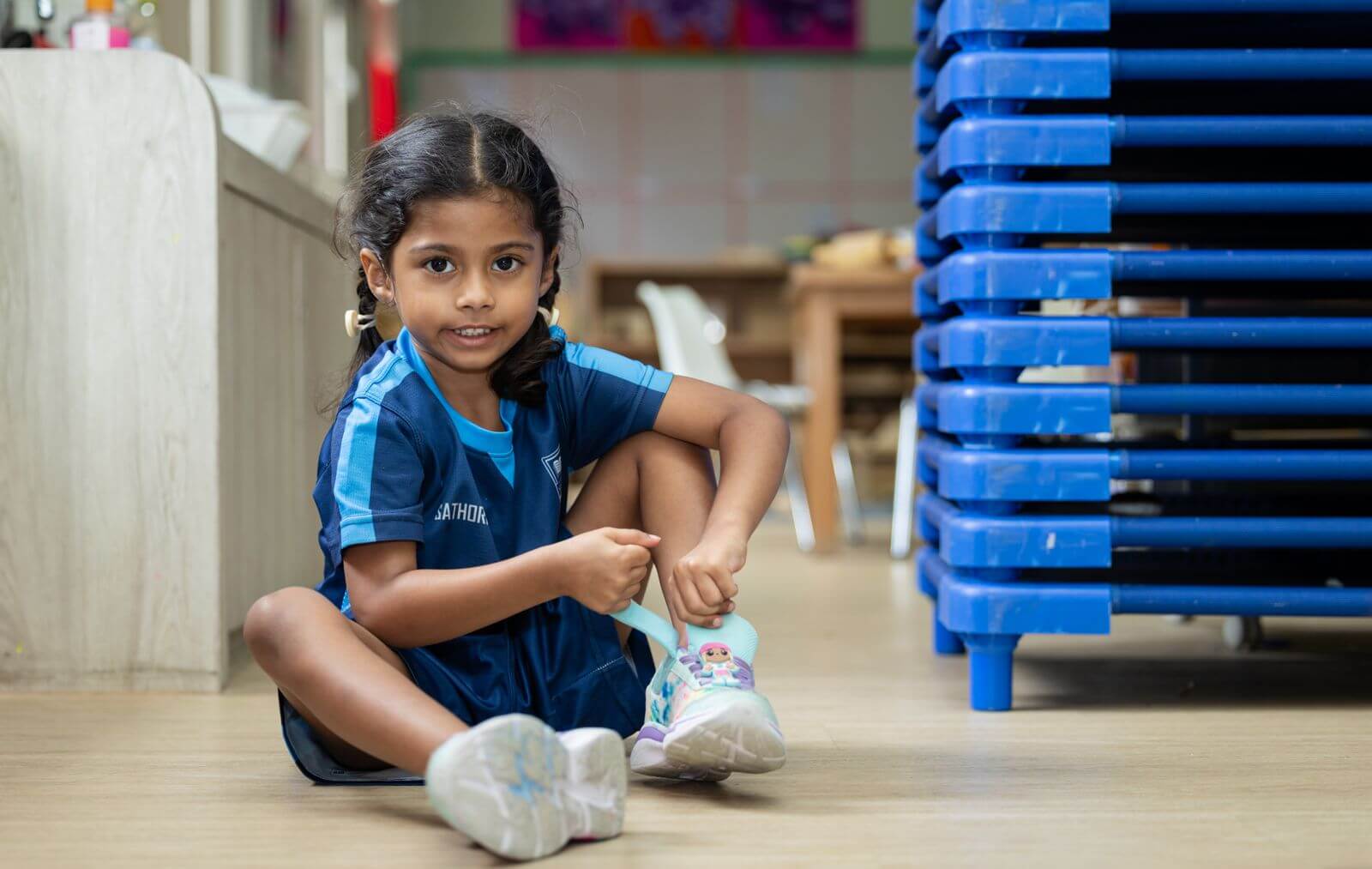 Early Years child putting on her own shoes, building independence at St. Andrews Sathorn